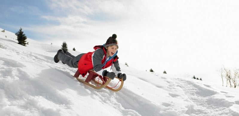 Boy On A Sled Playing In The Snow kids winter activities in Chamonix