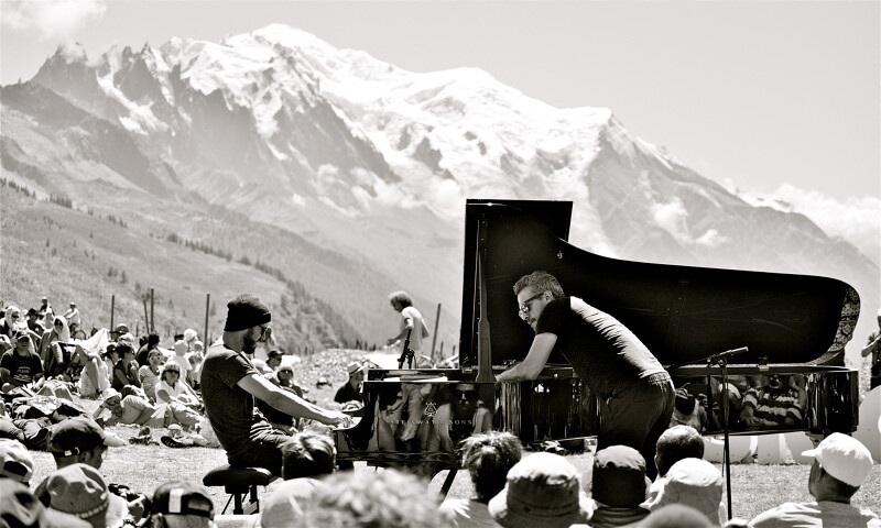 Black and white shot of musicians on a piano with a backdrop of the mountains 