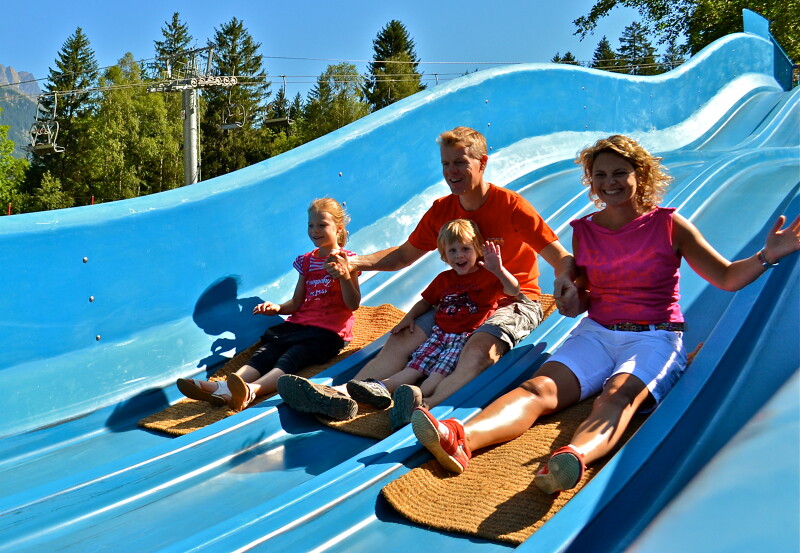 Photo of a family of 4 sliding down a big slide at a holiday park in the summer