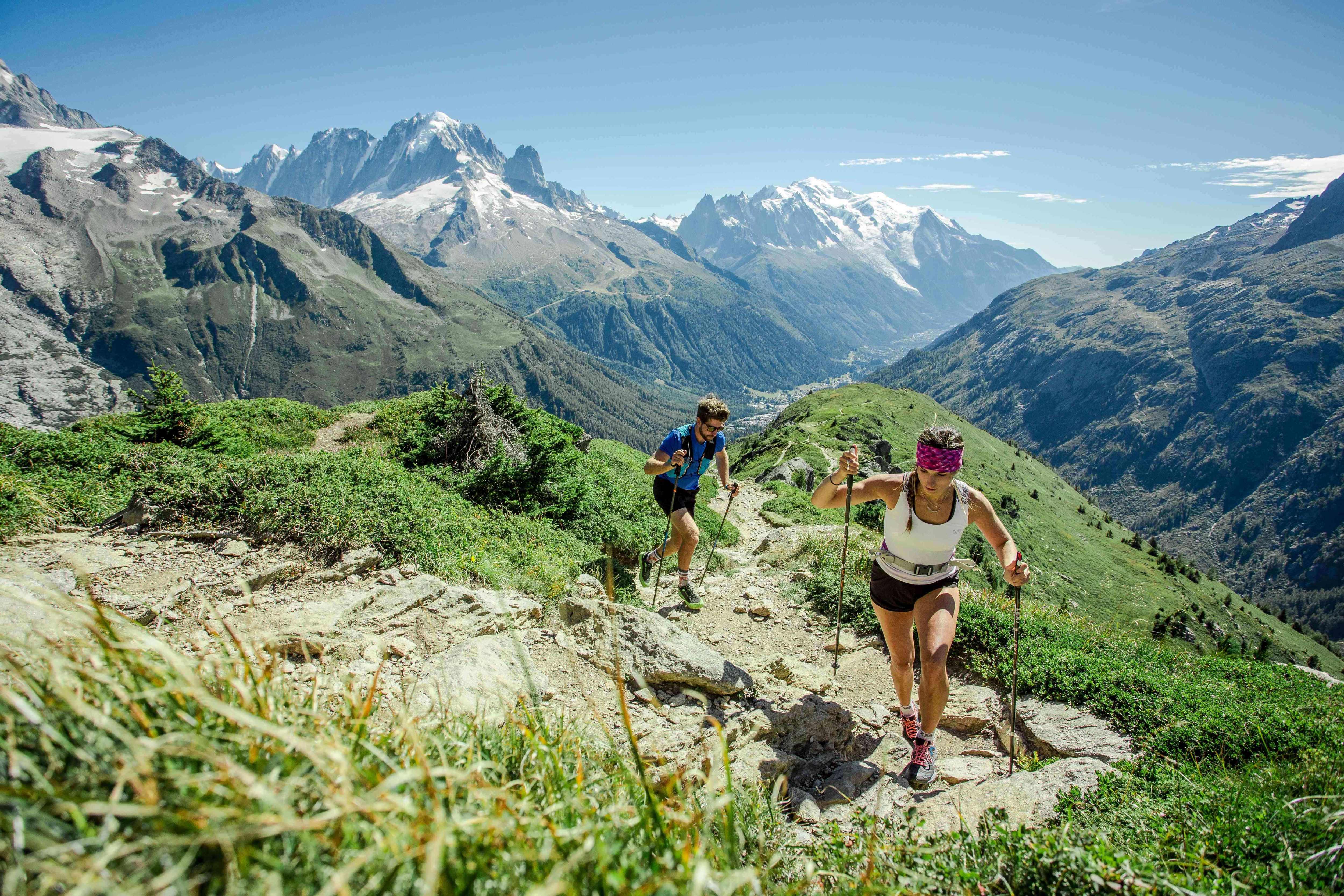 A man and a woman trail running up a mountain trail in the summer in Chamonix