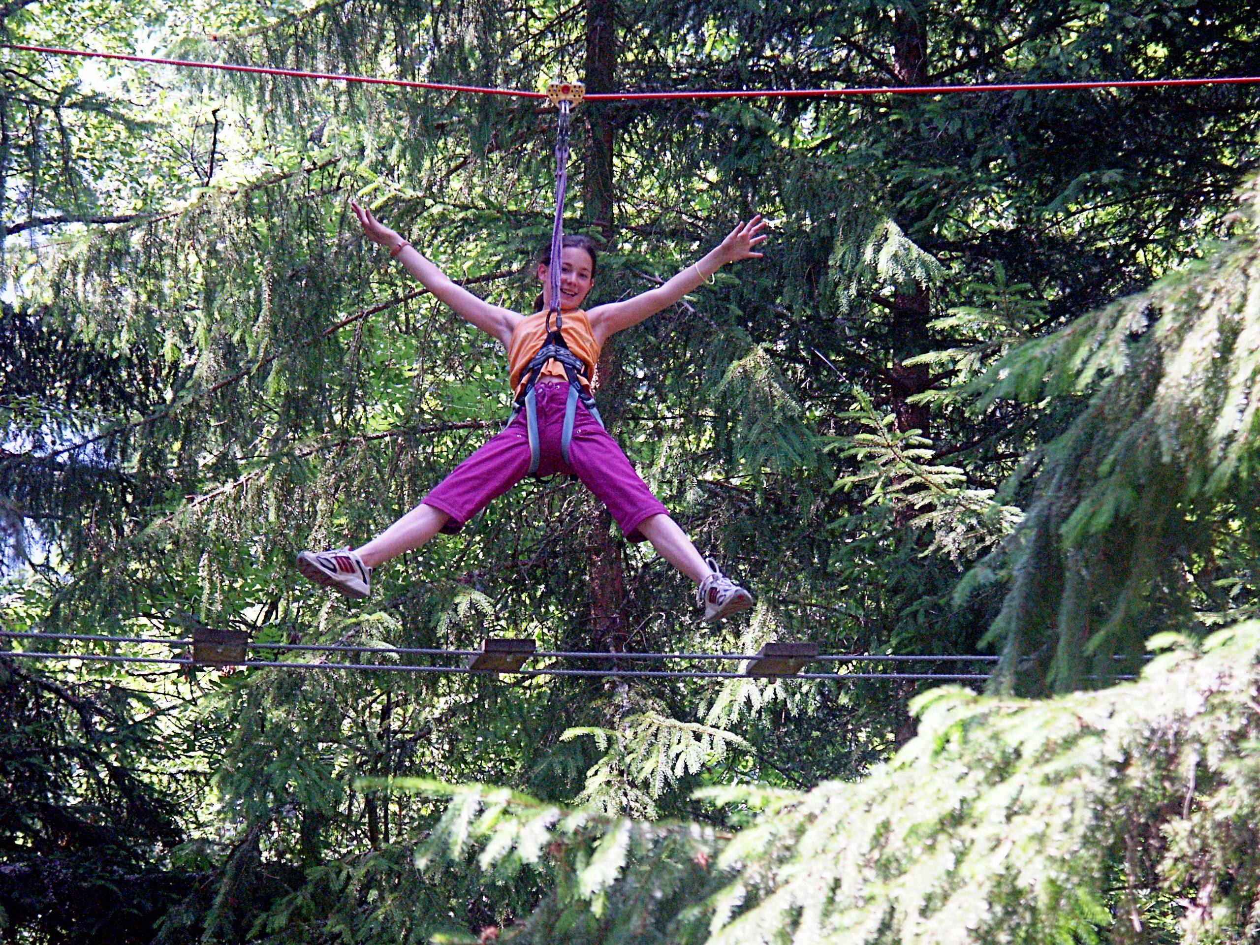 Young girl hanging in a harness from a tree rope amongst a forest on a sunny day