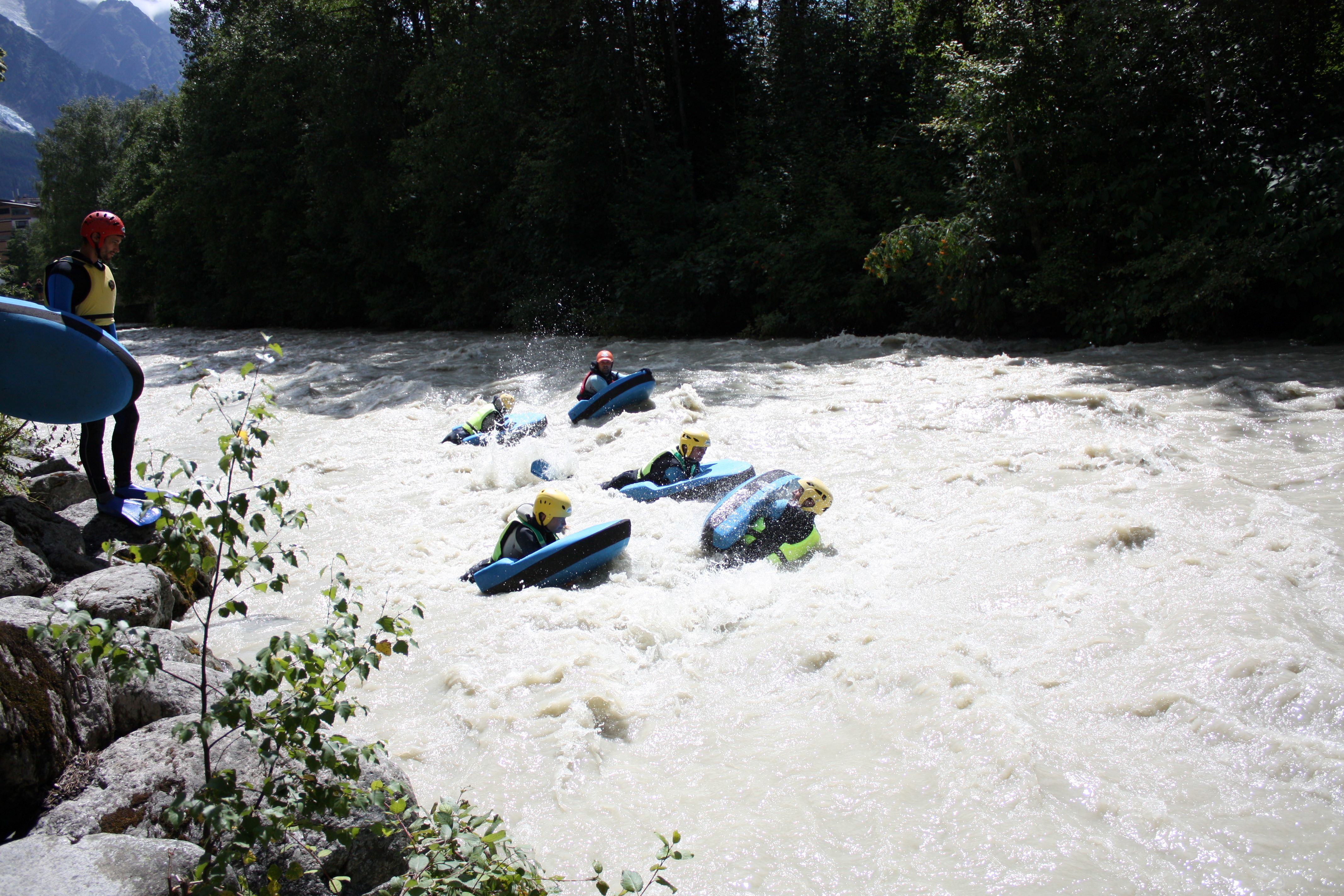 People body boarding through river rapids in wetsuits in the mountains 