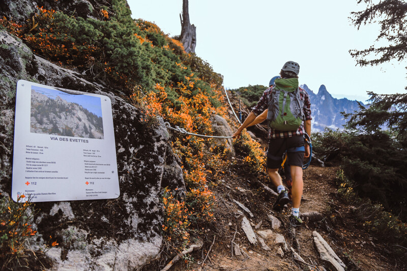 A person climbing up the side of a mountain holding on and clipped to a metal trail